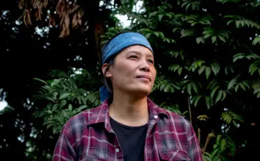 a vietnamese woman wearing a black t shirt, red flannel, and blue bandana around her forehead, standing in the forest