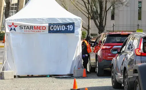 Vehicles line up next to a white tent that has a banner reading, "Starmed Healthcare COVID-19."