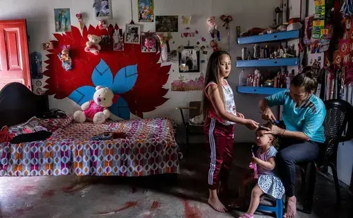 young girl stands in her room while her mom cuts hair of sibling