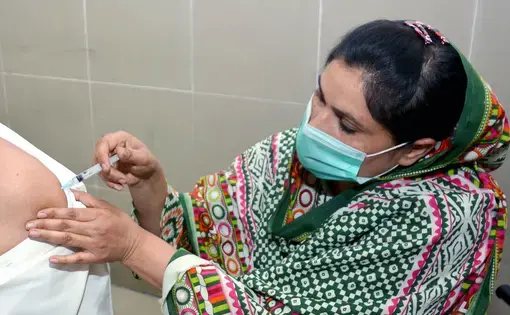 A health worker in PPE gives someone a vaccine.