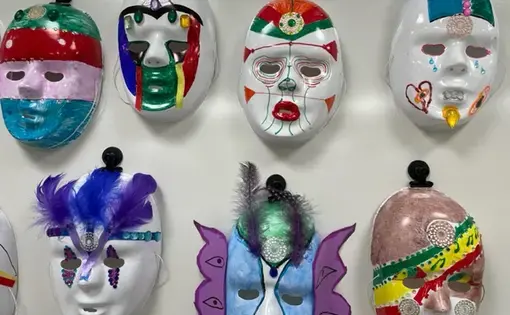 Seven student masks hang on a blank white wall.