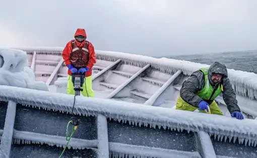 Men drill into ice that has accumulated on the deck of a ship