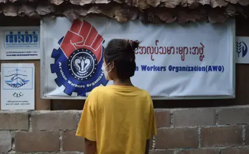 Woman stands masked in front of poster for Workers organization
