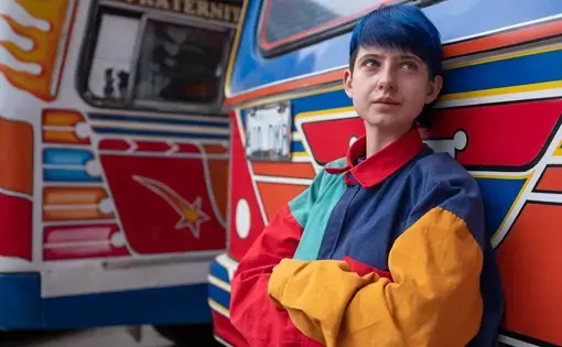 a young person leans against a colorful bus
