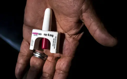 Naloxone spray in a hand glinting in a column of light.