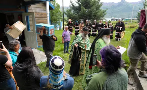 Two men carry painted boxes on their shoulders. People gather to watch.
