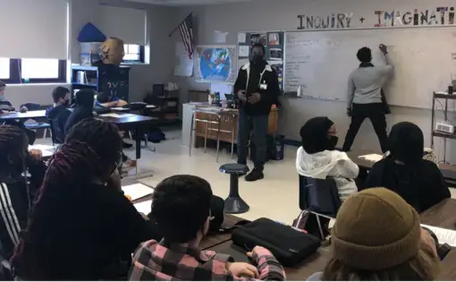 Students wearing mask face a white board, where a student is writing on the board