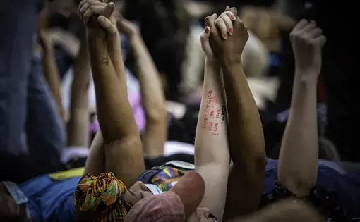 Protestors lie on the ground with their arms lifted and holding each others' hands.