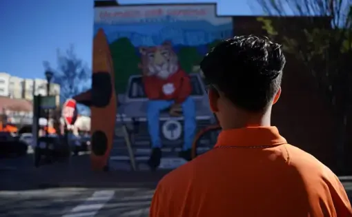 A young man crosses the street towards a mural with the Clemson Tiger mascot.