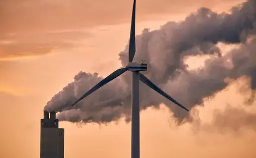A smoke tower releases gas next to a wind turbine- representing carbon dioxide emissions