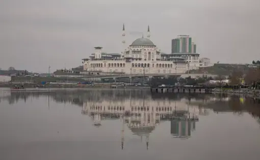 The façade of a mosque on the banks of a strait reflects on the water.