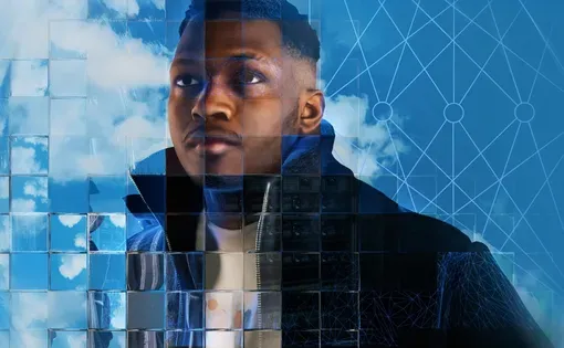 This image shows a young Black man wearing a black coat staring past the camera in front of a blue cloudy sky. The scene is refracted in different ways by a fragmented glass grid. This grid is a visual metaphor for the way that new artificial intelligence (AI) and machine learning technologies can be used to extract and analyse behavioural and demographic data in innovative ways.