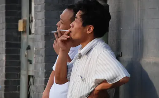 two men lean against a wall for a smoke break