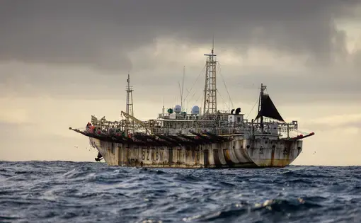 A fishing vessel floats on the open sea in cloudy weather