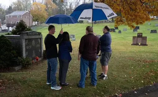 A group of people gather in a graveyard on a rainy day