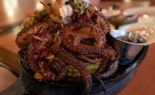 A restaurant-prepared plate of grilled whole octopus, topped with shrimp and chiles and placed in a hollowed-out pineapple