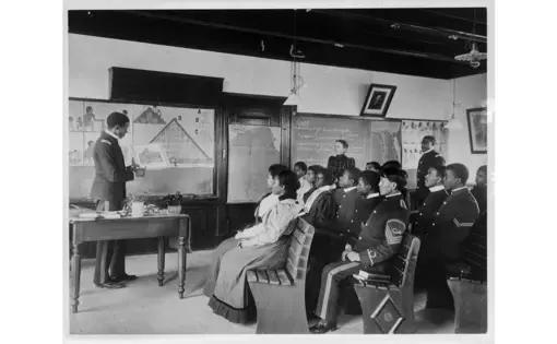 Black and Indigenous students in the U.s. look at a blackboard at Hampton Institute in 1899