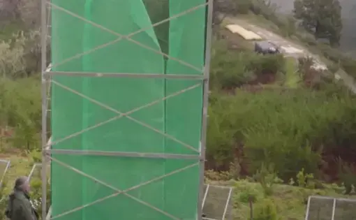 A green structure called a 'fog catcher' on the side of a lush foggy mountain