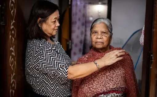 A woman appears to aid an older woman to put a shawl around her shoulders.