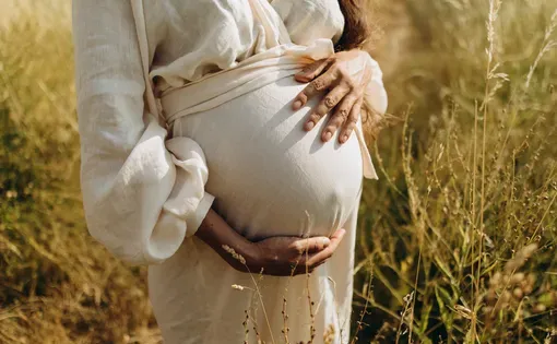a young woman in a white linen dress wrapped her arms around her pregnant belly. Image by Anne Ponomarenko/Shutterstock.