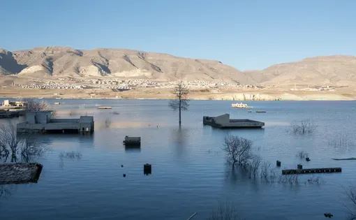 Boats sit on shady, still waters bordered by sandy white mountains.