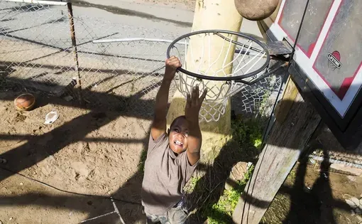 A young Black boy shoots a slam dunk in a basketball hoop