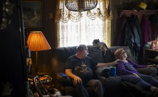 An couple sits snugly together on a sofa in a dim living room