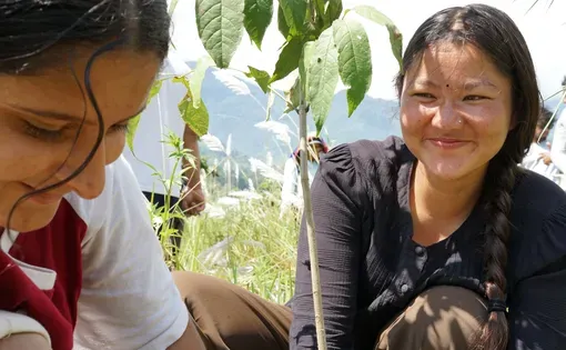 Mira Lamichhane (left) and Jaya Laxmi Kumai (right) plant trees by the river in the Lwang Valley as part of their community service component of the month-long Empowering Women of Nepal (EWN) female trekking guide training. They hope that these trees will help soak up flood water from the nearby river during the next storm. Image by Lauren Fox. Nepal, 2024.