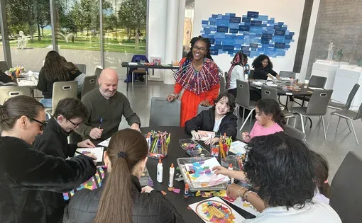 students and adults sit around a table creating art