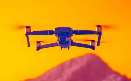 A drone equipped with special camera equipment flies above an orange sky and a pink mountain in the distance