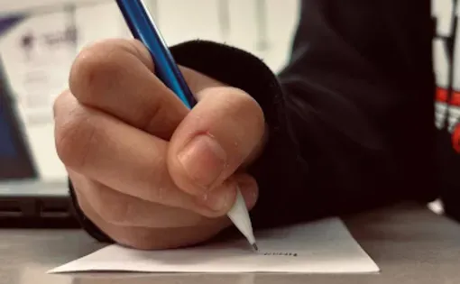 Close up image of student holding a pencil and writing on a sheet of paper