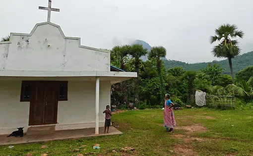 A white church sits on a field. A person on the left side of church looks on