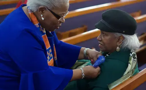 Joyce Elliott pins a ribbon on a congregant as the congregant sits on a church pew.