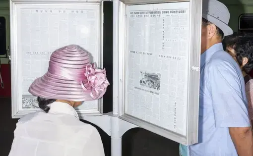 Commuters reading the official newspaper on a Pyongyang Metro platform.