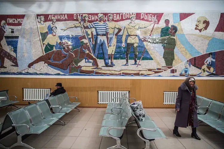 People wait for a train under a Soviet-era mural in Aralsk. Image&nbsp;by Taylor Weidman. Kazakhstan, 2017.
