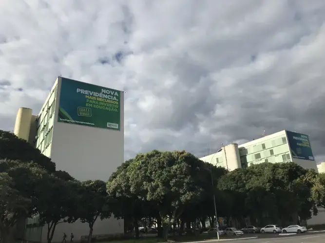 Government billboards at the top of each ministry building are promoting the benefits of approving a new social security system. The left billboard located atop the Education Ministry—where, in May, 2019,&nbsp;the federal education budget cuts were approved—reads 'The new social security. More resources to invest in education.' Image by Rafael Lima. Brazil, 2019.&nbsp;