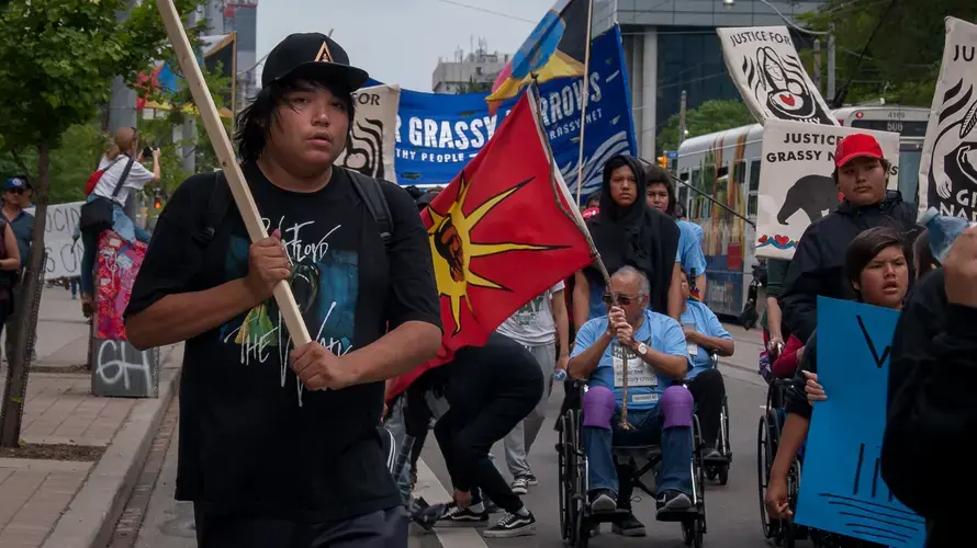 A Grassy Narrows youth, with a flag in his hand,&nbsp;helps to lead his community through the streets of Toronto. Canada, 2019. Image by Shelby Gilson.