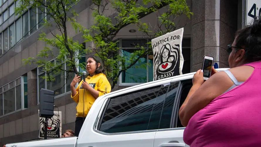 Jenae Turtle (left)&nbsp;stands before a crowd and speaks about her community while Chrissy Isaacs (right) stands below her, filming Jenae's speech. Canada, 2019. Image by Shelby Gilson.
