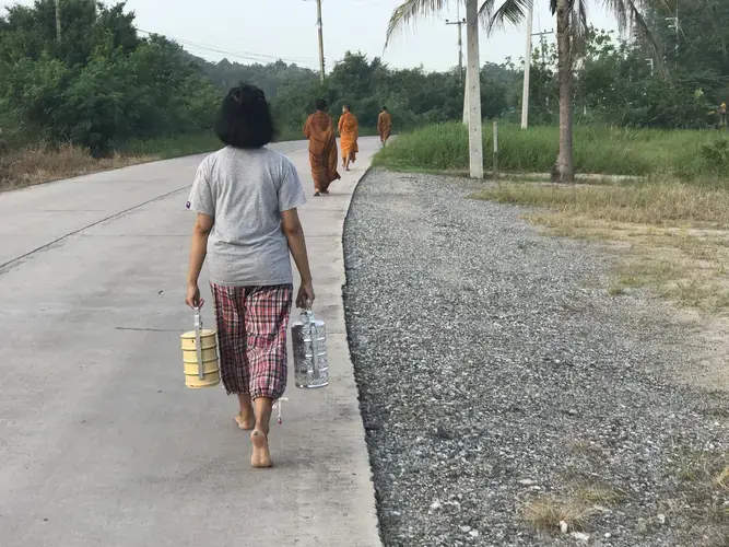 A young Thai girl follows three novice monks in the collection of the morning alms, during which they accept donations of food and drink to the temple from residents throughout the village of Chonburi. Image&nbsp;by Kiley Price. Thailand, 2018.
