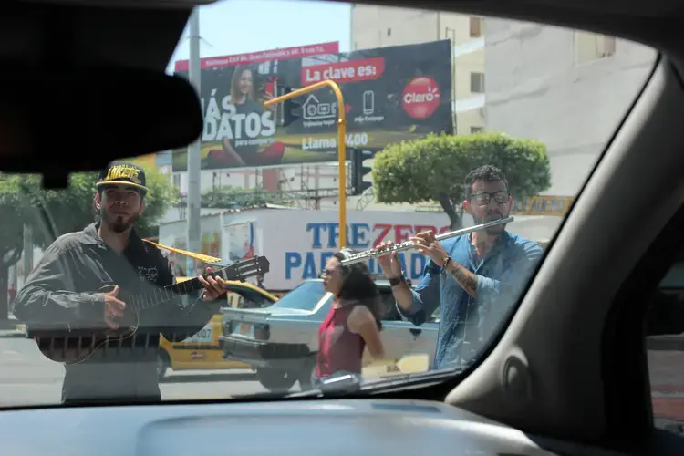 Venezuelans perform at a stoplight. One of them plays a popular Venezuelan instrument known for its four strings, a cuatro.&nbsp;Image by Mariana Rivas. Colombia, 2019.