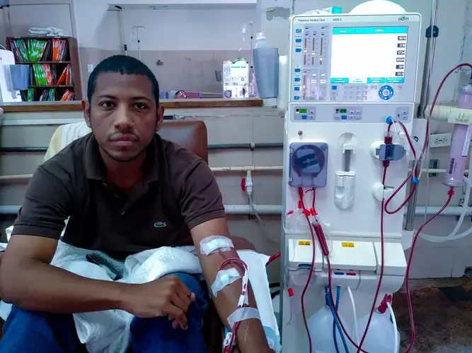 Wearing a brown shirt and a pair of blue jeans, Carlos Román sits down while connected to the dialysis machine at Clinica Riverside, in East Caracas. He receives dialysis three&nbsp;times a week during the morning shift, from 7 a.m. to 11 a.m. Image by Flaviana Sandoval. Venezuela, 2018.