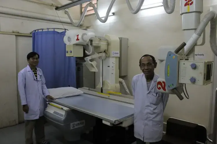 In Sihanouk Hospital Center of HOPE, in Phnom Penh, radiologists pose with one of the hospital's two donated X-ray machines. &nbsp;The hospital is an international charity with a creative operating model: the hospital receives international donations of medicine and equipment, and only charges patients for care that draws on resources that the hospital had to purchase; if diagnosis or treatment is undertaken with donated resources, then the patient isn’t charged. Image by M. G. Zimeta. Cambodia, 2018.