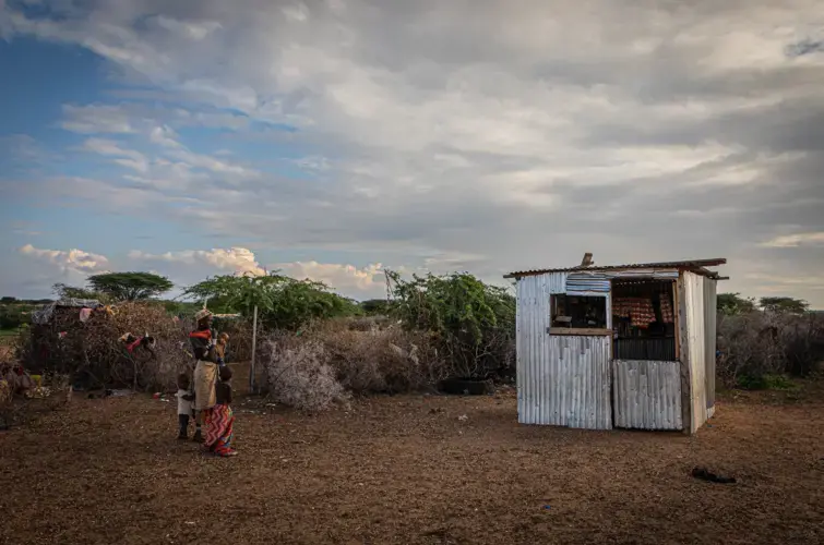 A young mother stands with her children outside a small stall in a village near Laisamis, Kenya.&nbsp;Image by Will Swanson. Kenya, 2020.