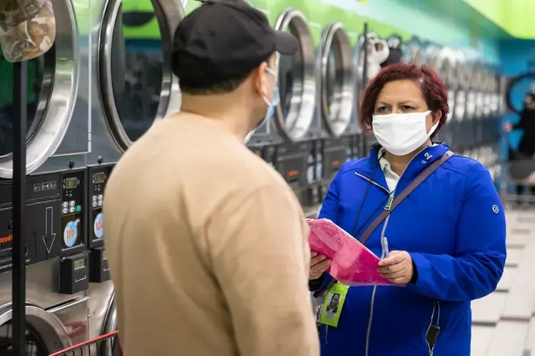 Margarita Sanchez, right, conducts a COVID-19 survey with a patron at a Belmont Cragin laundromat. Manuel Martinez / WBEZ News.<br />