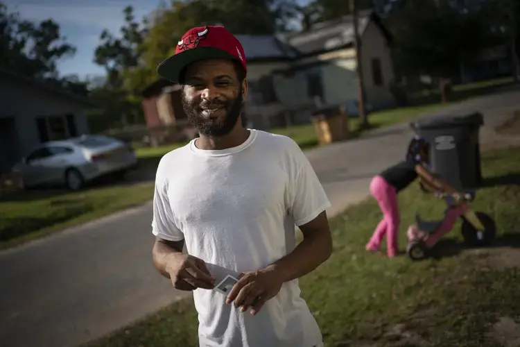 Demarkio Pritchett, 29, stands with his daughter Mariah Pritchett, 8, playing in the background outside his grandmother's home in Meridian, Miss. Image by Wong Maye-E / The Associated Press. United States, 2020.<br />