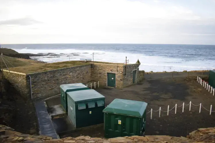 The EMEC wave test site substation at Billia Croo. The green boxes are transformers, that upscale power generated by devices in the water to the correct voltage for use on the island and national grid. None of the renewable energy generated at EMEC goes to waste. Image by Maggie More. United Kingdom, 2020.