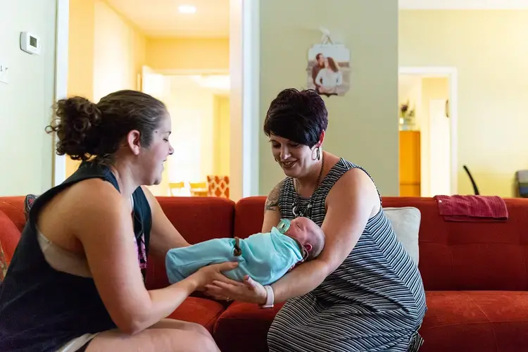 Hailey Frazier (left) gives her son Isaac to Sabrina Elliott (right), a doula in Abilene during a home visit.&nbsp;Image by Gary Rhodes for The Texas Tribune.&nbsp;United States, 2018.&nbsp;