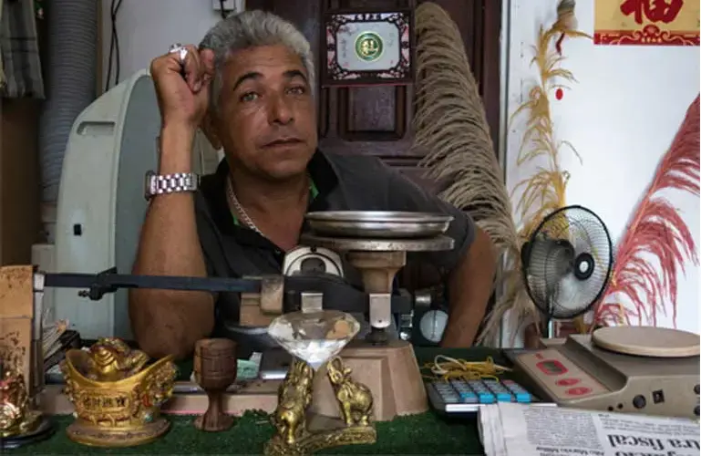A Tumeremo gold pawn shop owner sits behind his desk while enjoying the luxury of a cooling desk fan. He says that he is happy to buy and sell gold, and that it is far too dangerous to work in or around the mines. Image by Bram Ebus. Venezuela, 2017.<br />