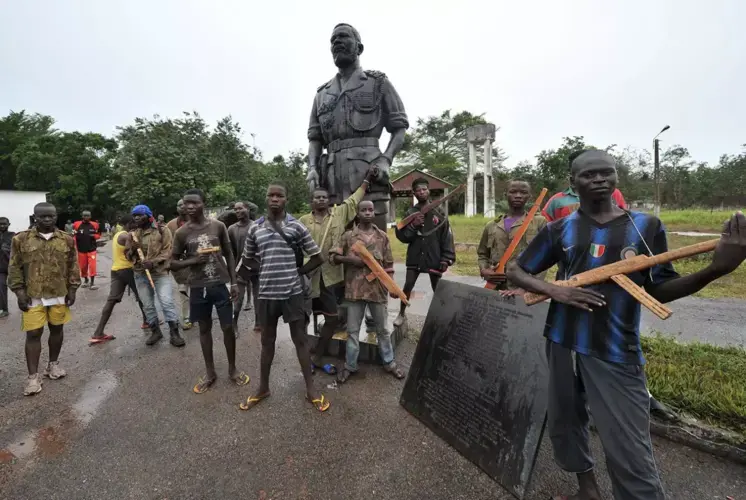 Ex-Seleka rebels with wooden weapons stand next to a statue of Emperor Bokassa at his Berengo palace in 2014. Image by Sia Kambou. Central African Republic, 2014.&nbsp;