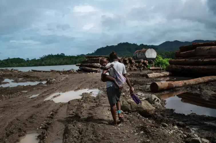 A woman walks through a logging point, used by the Apex company, on the eastern tip of Guadalcanal Island. Logging points like these are crucial for moving round logs to ships, and out of the country. Image by Monique Jaques. Solomon Islands, 2020.